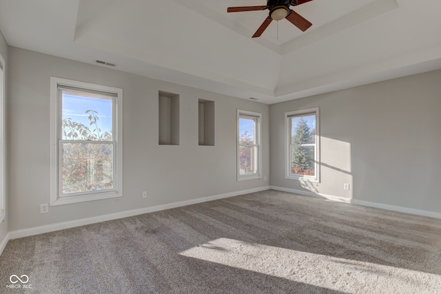 carpeted empty room featuring ceiling fan, a tray ceiling, and a wealth of natural light