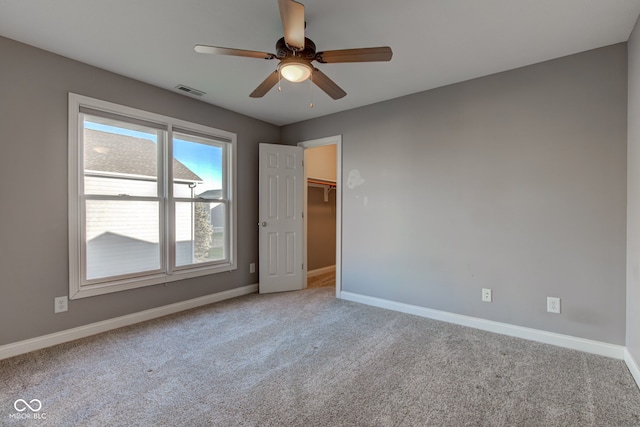 unfurnished bedroom with a closet, a spacious closet, carpet, and ceiling fan