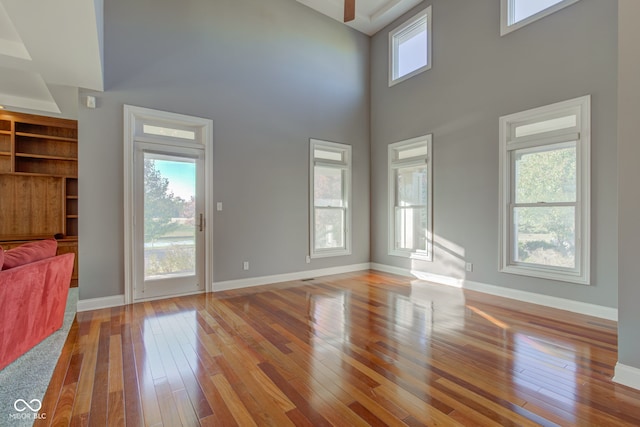 unfurnished living room with light hardwood / wood-style floors, a towering ceiling, and plenty of natural light