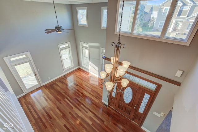 foyer with hardwood / wood-style floors, ceiling fan with notable chandelier, and a high ceiling