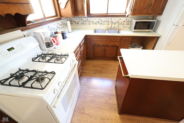 kitchen featuring light wood-type flooring, a healthy amount of sunlight, white gas stove, and sink