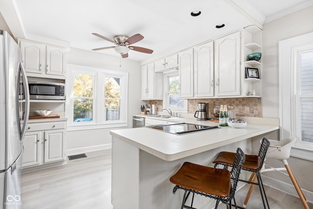 kitchen featuring a kitchen breakfast bar, kitchen peninsula, white cabinets, appliances with stainless steel finishes, and tasteful backsplash