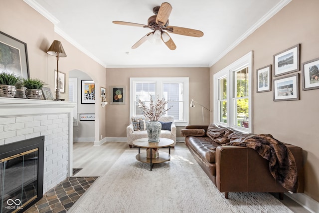 living room featuring crown molding, ceiling fan, a brick fireplace, and dark hardwood / wood-style flooring