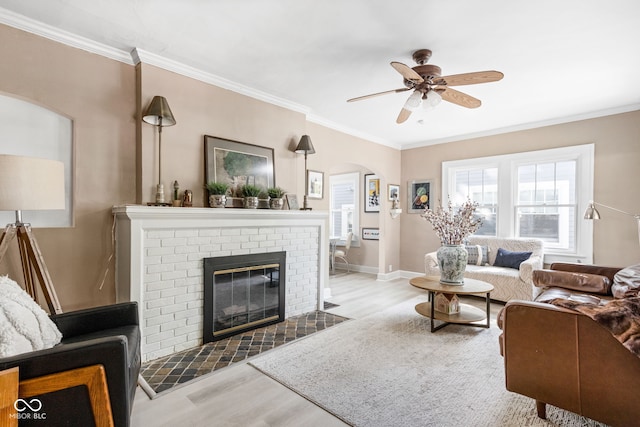 living room featuring ceiling fan, ornamental molding, light wood-type flooring, and a fireplace