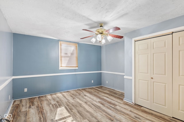 unfurnished bedroom featuring light hardwood / wood-style flooring, a textured ceiling, a closet, and ceiling fan