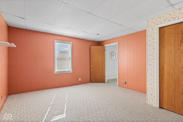 unfurnished room with a drop ceiling, wood walls, and carpet flooring