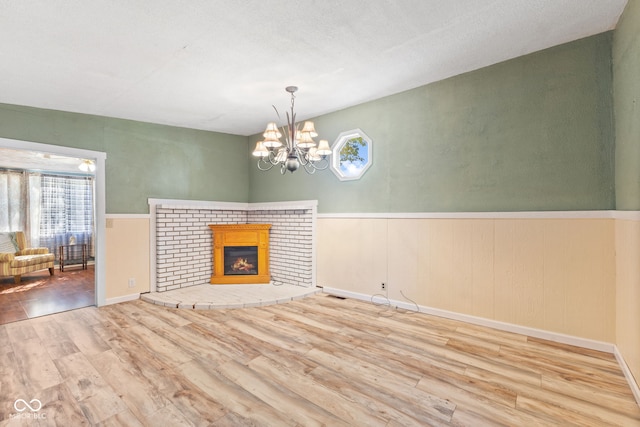 unfurnished living room with a textured ceiling, wood-type flooring, an inviting chandelier, and a brick fireplace