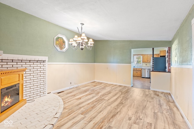 unfurnished dining area featuring lofted ceiling, a textured ceiling, a chandelier, light hardwood / wood-style flooring, and a fireplace