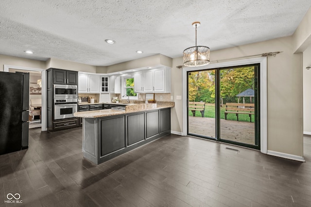 kitchen featuring kitchen peninsula, black fridge, white cabinetry, decorative light fixtures, and light stone counters