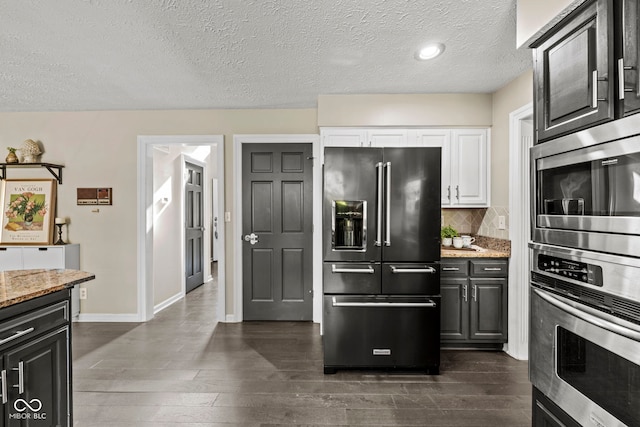 kitchen with dark hardwood / wood-style floors, light stone countertops, white cabinets, appliances with stainless steel finishes, and a textured ceiling