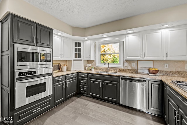 kitchen featuring sink, white cabinetry, appliances with stainless steel finishes, light stone counters, and light hardwood / wood-style floors