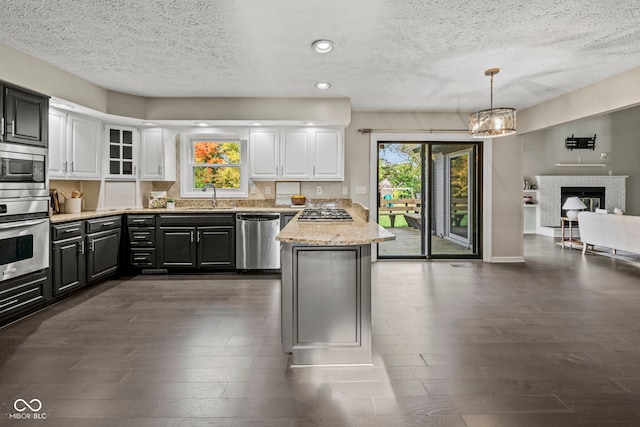 kitchen with white cabinetry, a tiled fireplace, a healthy amount of sunlight, and appliances with stainless steel finishes