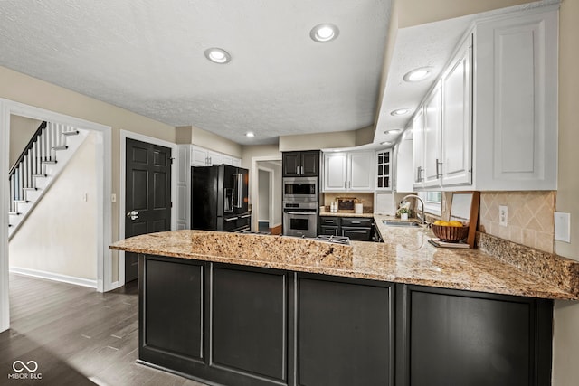 kitchen with white cabinetry, black refrigerator with ice dispenser, kitchen peninsula, and sink