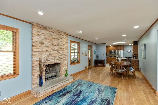 living room with light hardwood / wood-style floors, ornamental molding, and a stone fireplace