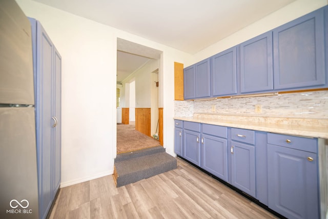 kitchen featuring blue cabinets, decorative backsplash, light hardwood / wood-style floors, and stainless steel refrigerator