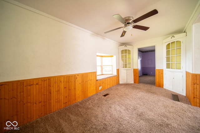 spare room featuring ornamental molding, wooden walls, carpet, and ceiling fan