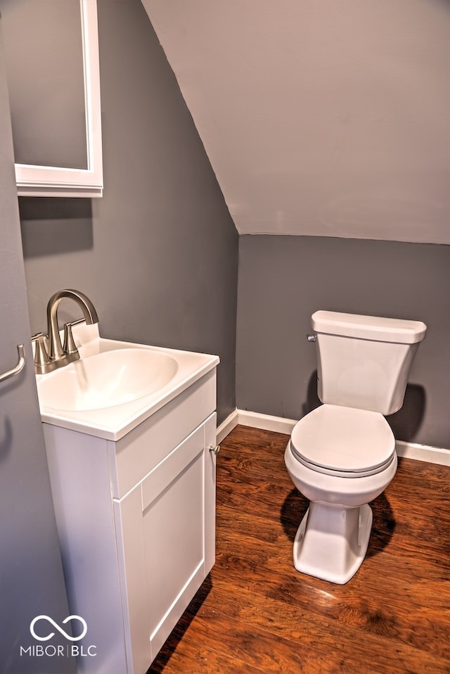 bathroom featuring vanity, hardwood / wood-style floors, vaulted ceiling, and toilet