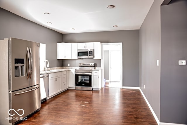 kitchen featuring appliances with stainless steel finishes, sink, white cabinetry, dark wood-type flooring, and light stone counters