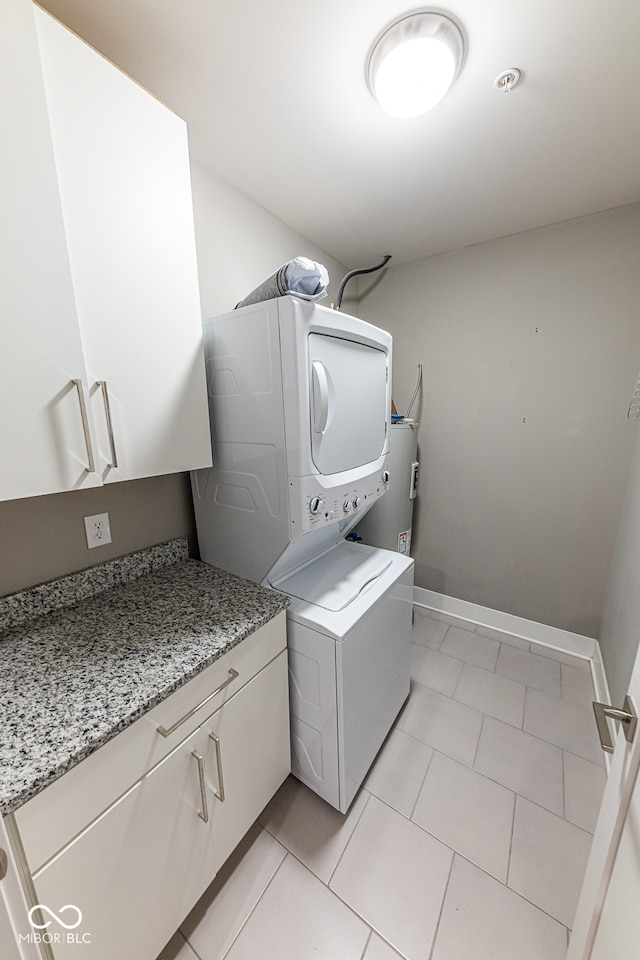 laundry area with water heater, stacked washer / dryer, cabinets, and light tile patterned flooring