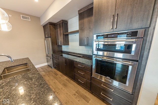 kitchen featuring sink, light hardwood / wood-style flooring, stainless steel appliances, and dark stone countertops