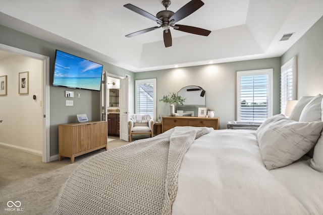 bedroom with ensuite bath, light colored carpet, a tray ceiling, and ceiling fan