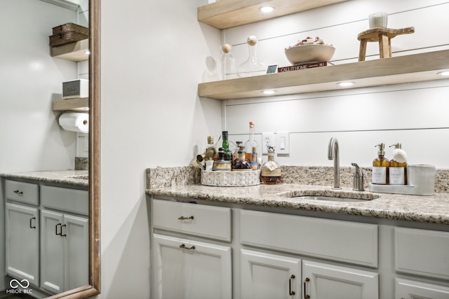 bar with gray cabinetry, light stone counters, and sink