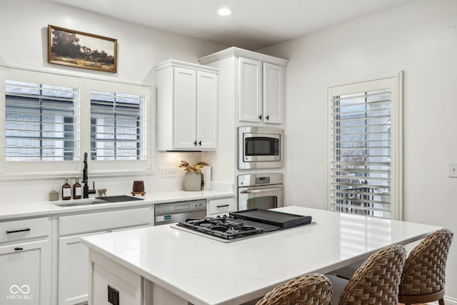 kitchen with a breakfast bar area, white cabinetry, stainless steel appliances, sink, and a center island