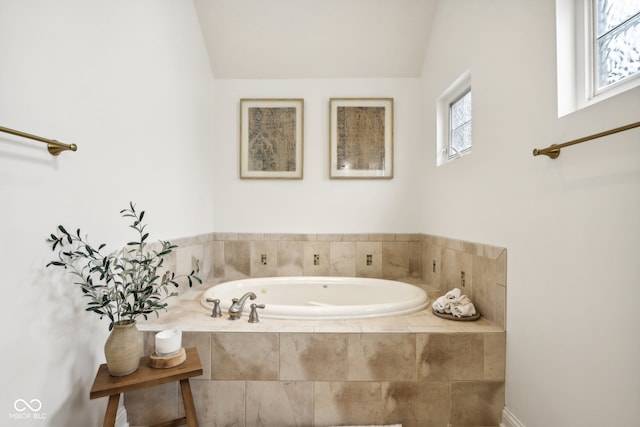 bathroom featuring a wealth of natural light, vaulted ceiling, and tiled tub