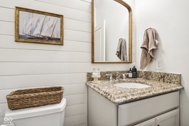 bathroom featuring toilet, wood walls, and vanity