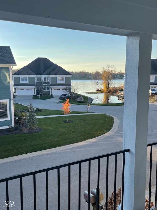 yard at dusk with a balcony, a garage, and a water view