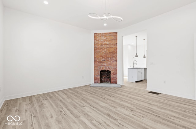 unfurnished living room featuring sink, a brick fireplace, and light wood-type flooring