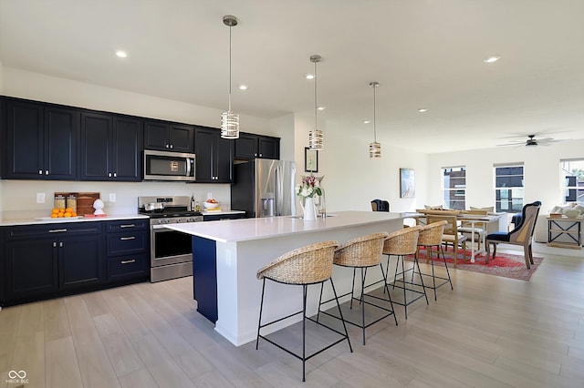 kitchen featuring a kitchen island, a kitchen breakfast bar, light hardwood / wood-style floors, stainless steel appliances, and pendant lighting