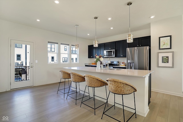 kitchen with an island with sink, light hardwood / wood-style floors, stainless steel appliances, decorative light fixtures, and a breakfast bar area