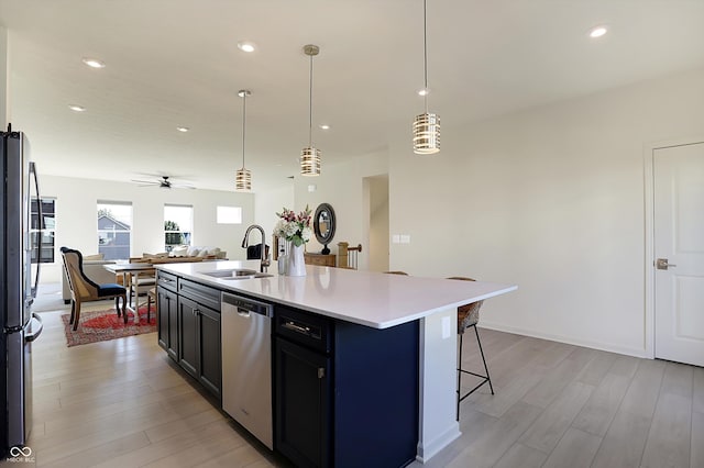 kitchen with a center island with sink, sink, stainless steel appliances, and light wood-type flooring