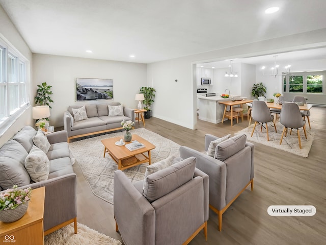 living area with baseboards, light wood-type flooring, recessed lighting, and a notable chandelier