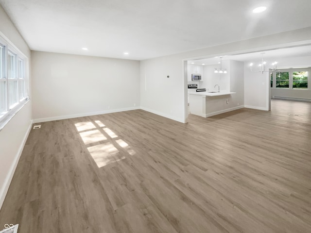 unfurnished living room featuring baseboard heating, sink, hardwood / wood-style floors, and a chandelier