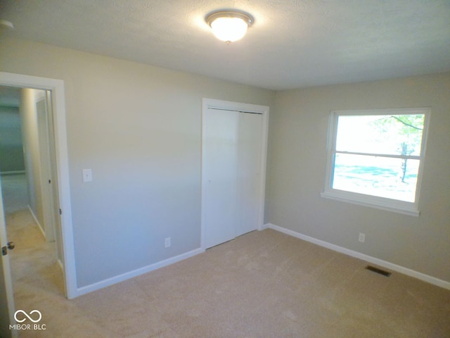 unfurnished bedroom featuring a closet, a textured ceiling, and light colored carpet