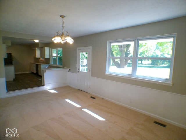 unfurnished dining area featuring light carpet and a chandelier