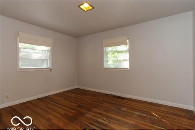 empty room featuring a wealth of natural light and dark wood-type flooring