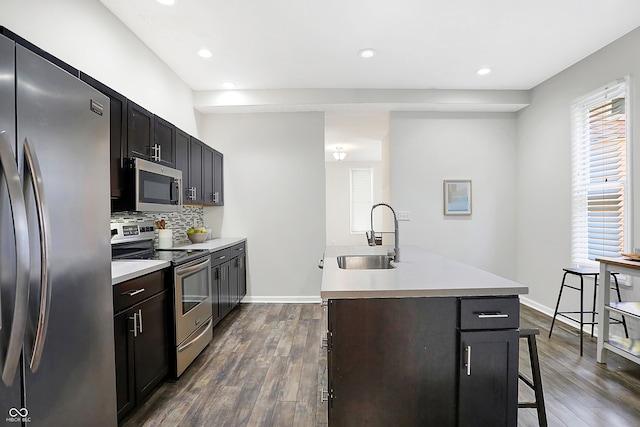 kitchen with dark hardwood / wood-style floors, stainless steel appliances, sink, and an island with sink