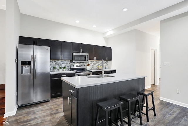 kitchen with a center island with sink, tasteful backsplash, appliances with stainless steel finishes, a kitchen breakfast bar, and dark hardwood / wood-style floors