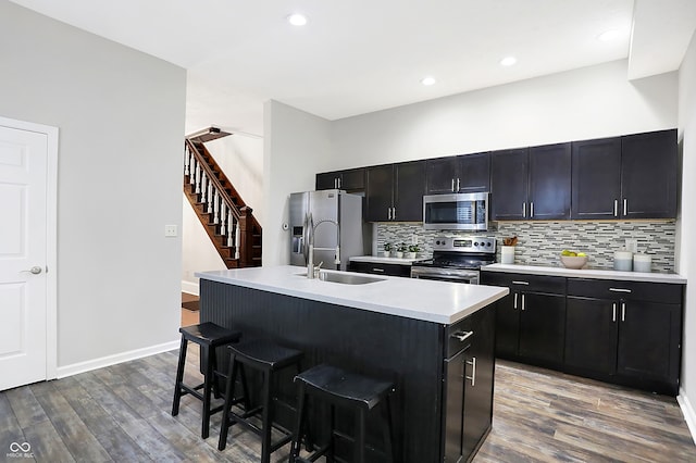 kitchen with stainless steel appliances, an island with sink, a kitchen breakfast bar, and hardwood / wood-style floors