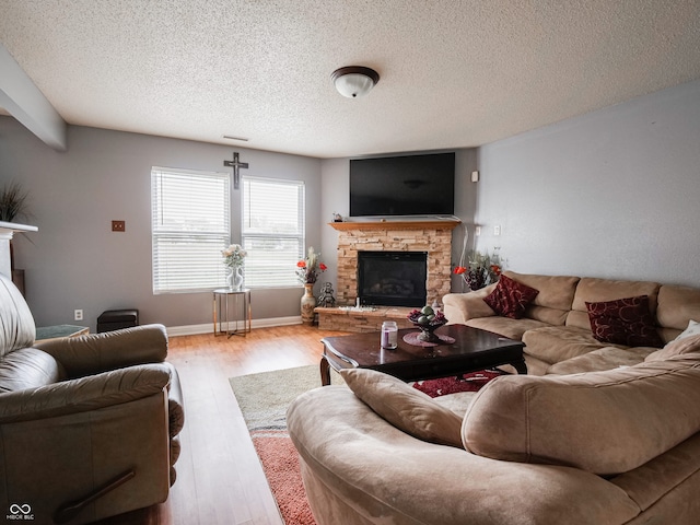 living room featuring light hardwood / wood-style floors, a stone fireplace, and a textured ceiling