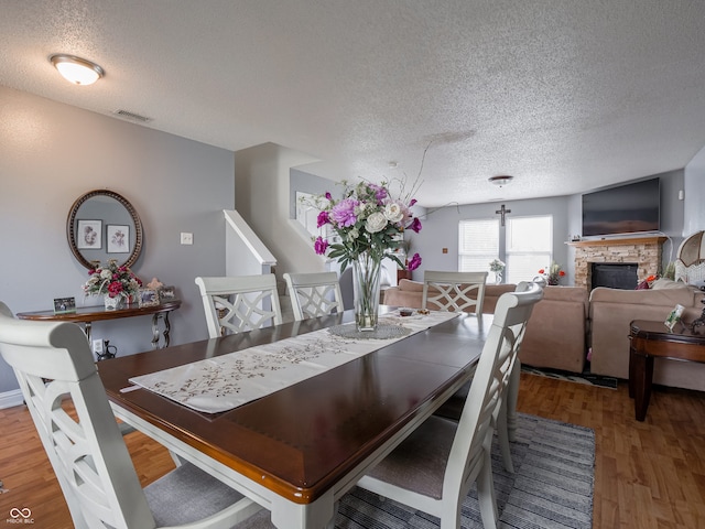 dining room featuring a stone fireplace, a textured ceiling, and hardwood / wood-style flooring