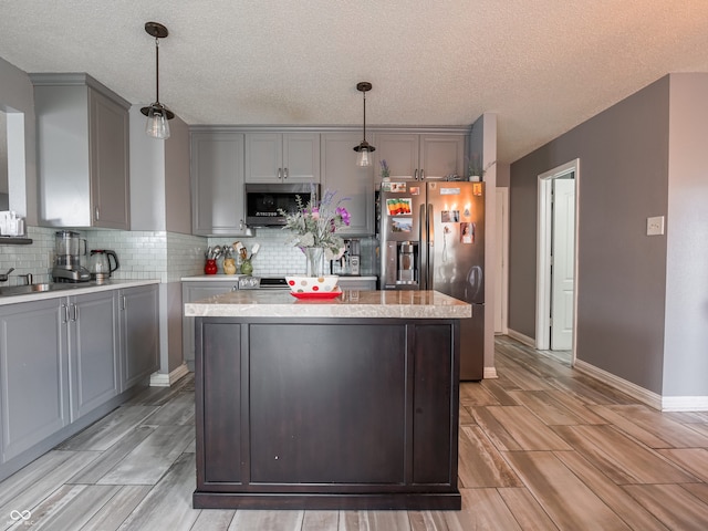 kitchen with gray cabinets, a textured ceiling, stainless steel appliances, and hanging light fixtures