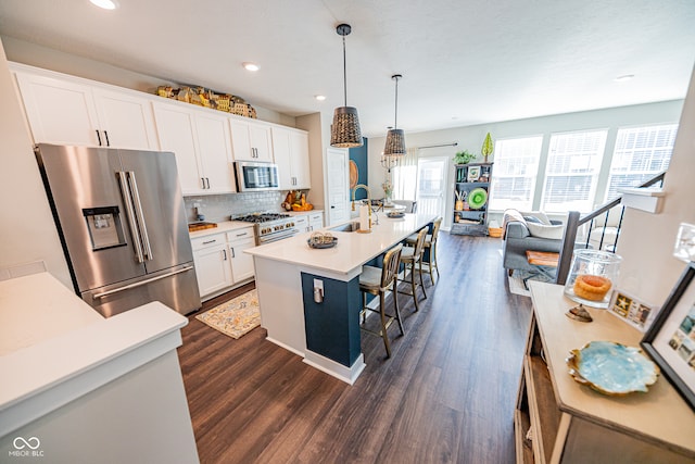 kitchen featuring dark wood-type flooring, stainless steel appliances, a center island with sink, decorative light fixtures, and white cabinets