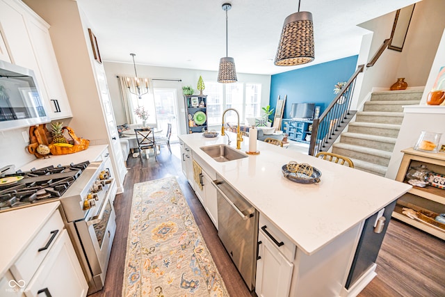 kitchen featuring a kitchen island with sink, stainless steel appliances, sink, pendant lighting, and white cabinetry