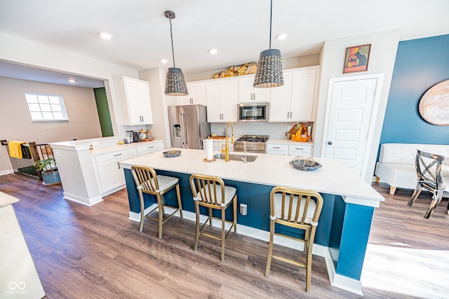 kitchen with white cabinets, an island with sink, hardwood / wood-style flooring, pendant lighting, and stainless steel appliances