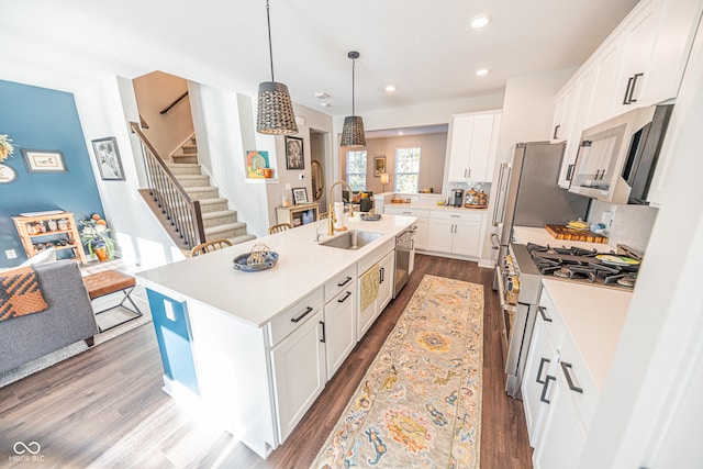 kitchen featuring sink, hanging light fixtures, white cabinetry, stainless steel appliances, and a center island with sink