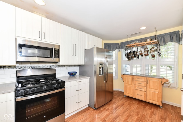 kitchen with white cabinetry, light hardwood / wood-style floors, tasteful backsplash, and appliances with stainless steel finishes